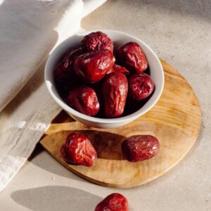 A ceramic bowl filled with red dates on a wooden board, casting soft shadows.